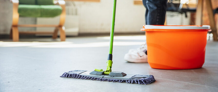 A mop is on the floor next to an orange cup.