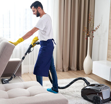 A man in blue shirt and yellow apron holding vacuum cleaner.