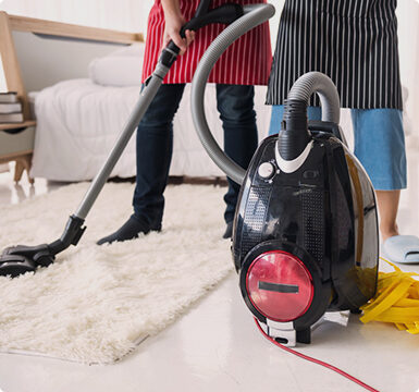 A man and woman are vacuuming the floor.