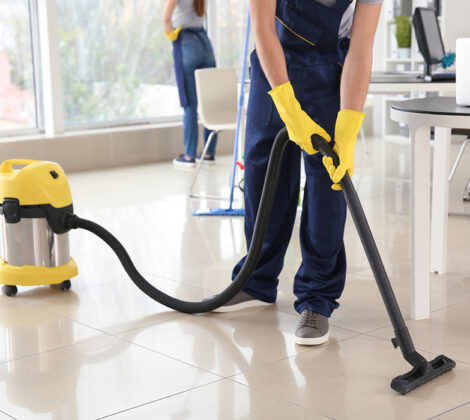 A person in yellow gloves vacuuming the floor.