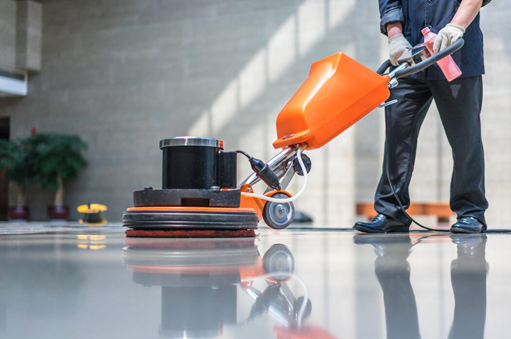 A man is cleaning the floor with an orange machine.